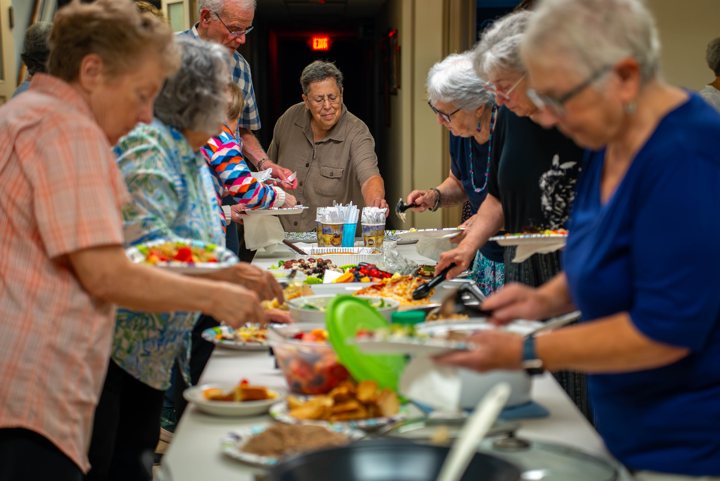 People share food around a long buffet table.