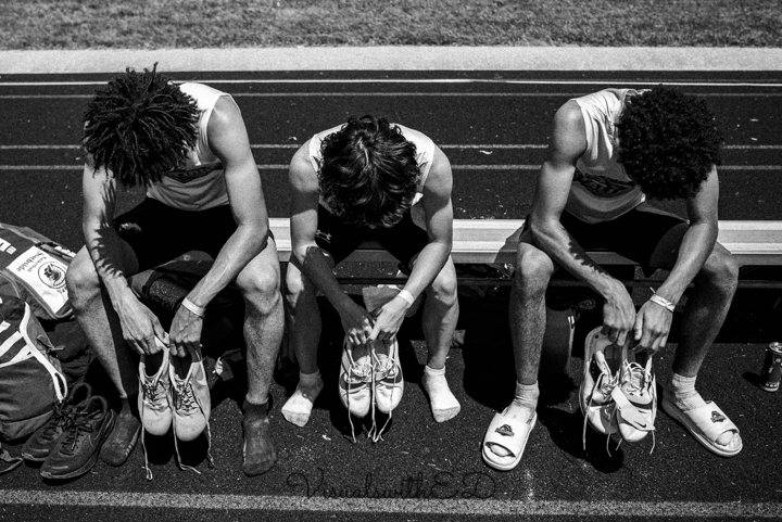 Black-and-white photograph of three athletes seated with their running shoes.