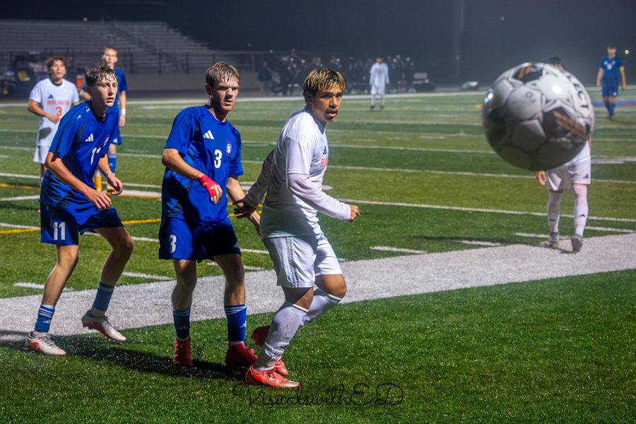 Soccer players watch an airborne ball during a night match.