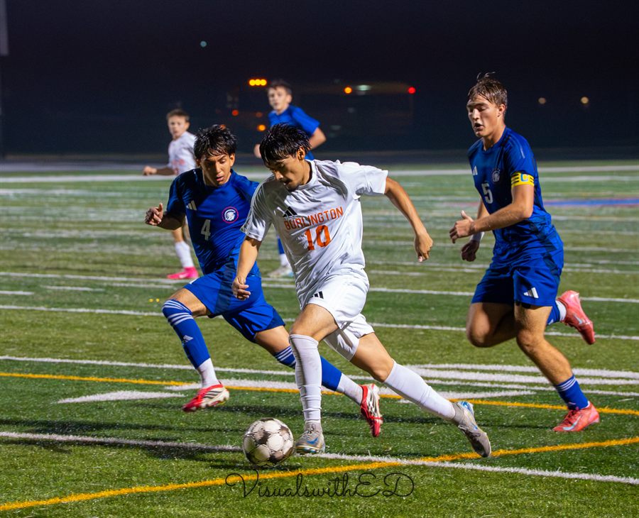 A player in white shields the ball as two blue-shirted opponents close in.