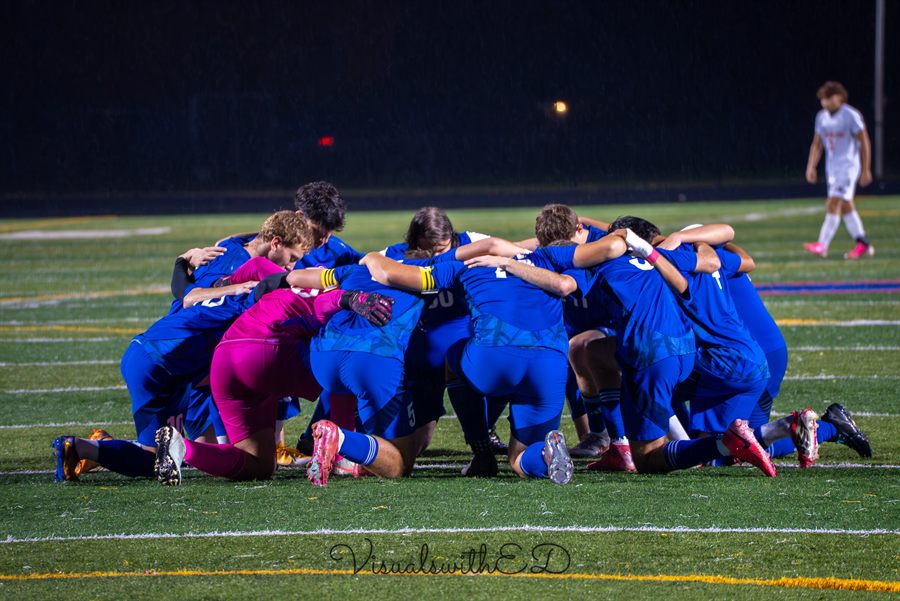 Players in blue gather in a celebratory huddle on the soccer field.